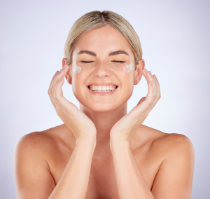 beauty-face-happy-woman-with-cream-application-facial-hydration-dermatology-glowing-skincare-studio-lotion-person-smile-success-acne-prevention-product-grey-background